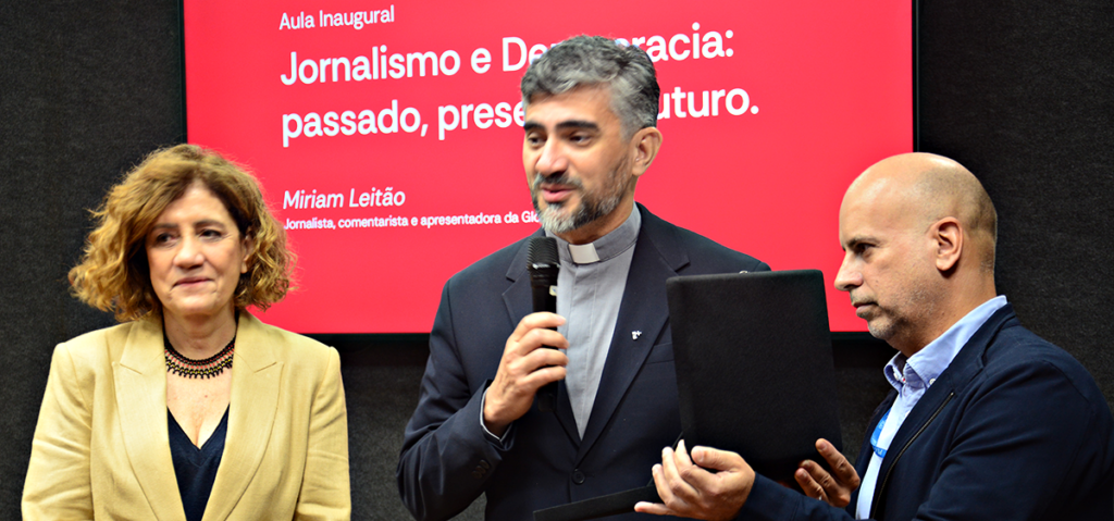 O Reitor da PUC-Rio, Padre Anderson Antonio Pedroso, S.J., entrega a homenagem para a jornalista Miriam Leitão, ao lado do diretor do DCOM, professor Arthur Ituassu. Foto: Alícia Souza